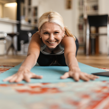 Eine Frau macht Yoga auf einer Yoga Matte im Wohnzimmer.