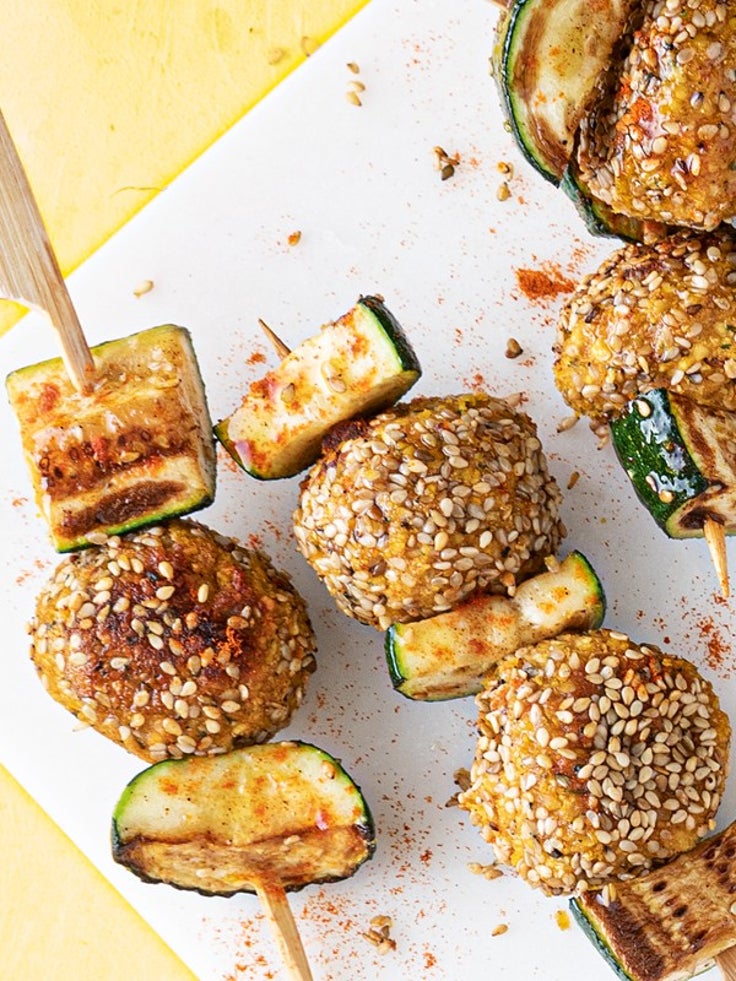 Falafelspieße mit Zucchini und Sesam auf einem hellen Teller, bestreut mit Paprikagewürz auf gelbem Untergrund.