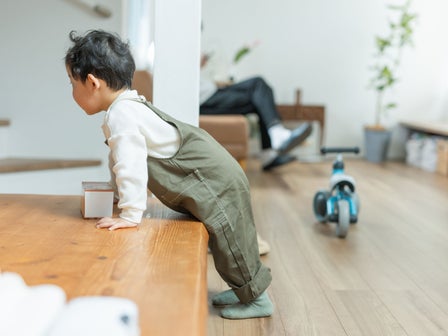Kleinkind steht im Wohnzimmer an einer niedrigen Bank und übt selbstständig das Hochziehen