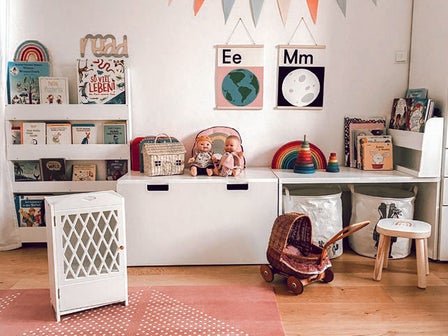 Aufgeräumtes Kinderzimmer mit Bücherregal, Kommoden, Ablagen, kleinem Puppenwagen und Spielzeug