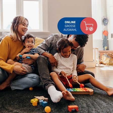 Eine Familie sitzt im Wohnzimmer auf dem Boden und lacht.