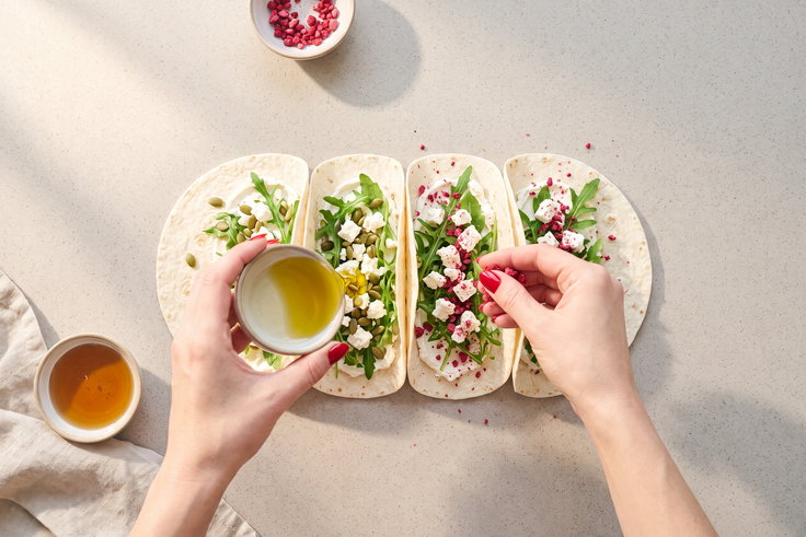 Mini Wraps mit Feta, Rucola und Kürbiskernen werden mit Olivenöl, Agavendicksaft und zerbröselten Himbeeren verfeinert.