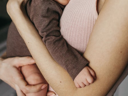 Eine Frau hält ein schlafendes Baby eng an ihrer Brust, das friedlich auf ihrer Schulter liegt.