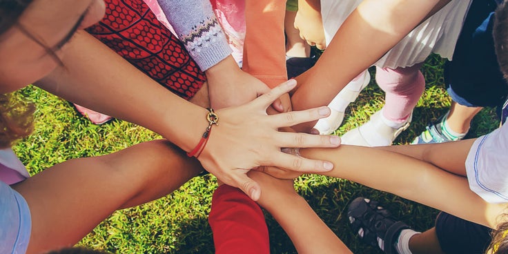 Auf der Grafik sind die Arme und Hände von mehreren im Kreis stehenden Personen zu sehen, die sich in der Mittag berühren