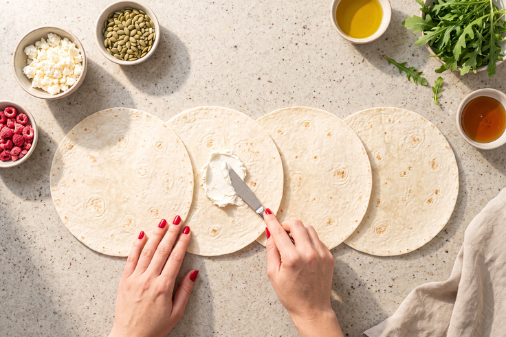 Tortilla-Wraps werden für Mini Wraps mit Feta, Rucola und Himbeer-Topping mit Frischkäse bestrichen.
