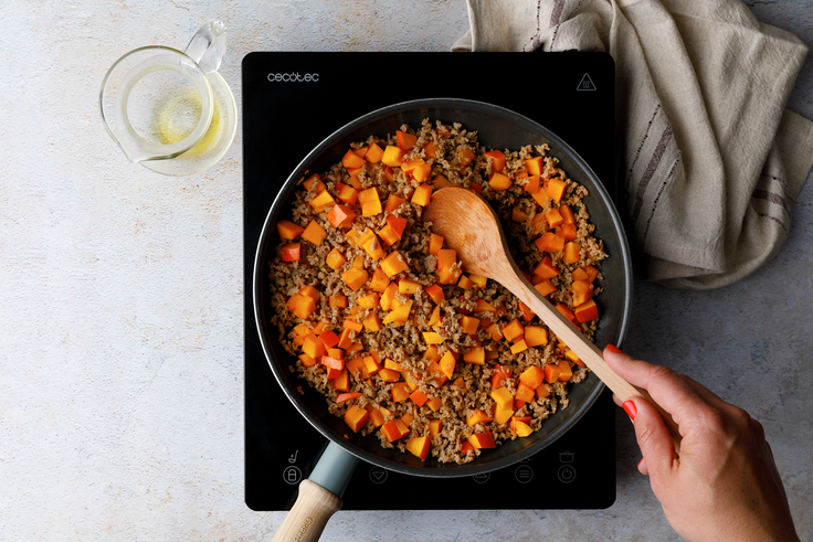 Veggiehack und Kürbiswürfel werden für Protein Linsen-Spirelli mit Bohnensauce in einer Pfanne auf einer Kochplatte angebraten.