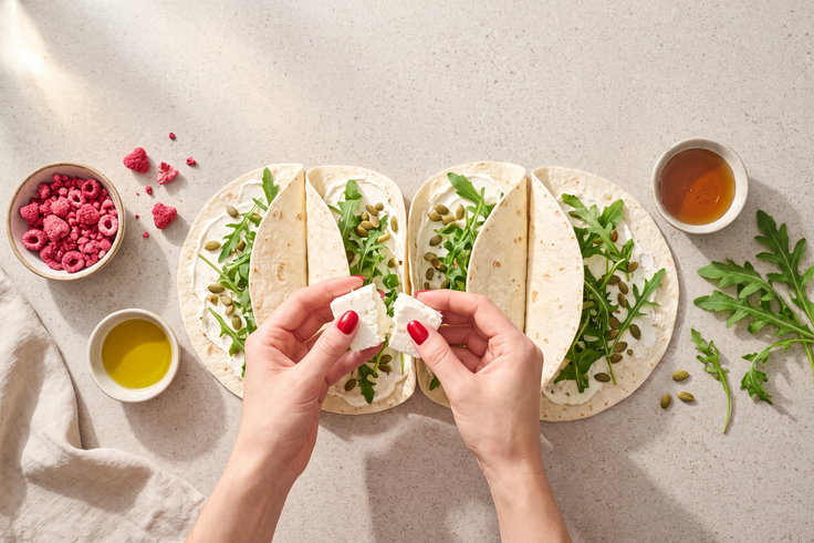 Tortilla-Wraps werden für Mini Wraps mit Feta, Rucola und Himbeer-Topping mit Rucola, Kürbiskernen und Feta belegt.