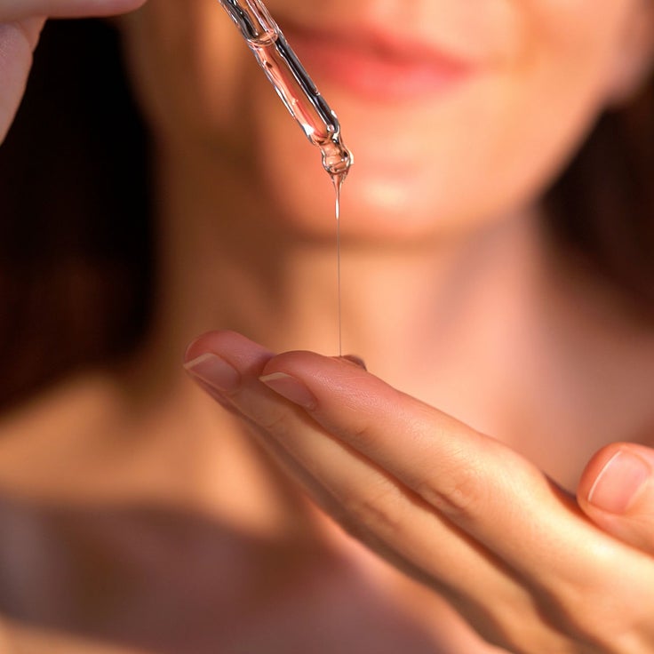 Frau gibt mit einer Pipette Serum auf ihre Handfläche als Schritt einer reduzierten Japanese Beauty Pflegeroutine.