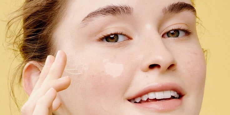 Person mit nackten Schultern berührt sanft ihre Wange vor gelbem Hintergrund und veranschaulicht das Ergebnis einer gepflegten Haut nach einer Korean Skincare Routine