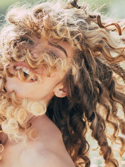 Zur Curly-Girl-Methode: Lachende Frau mit langen, natürlichen Locken im Sonnenlicht