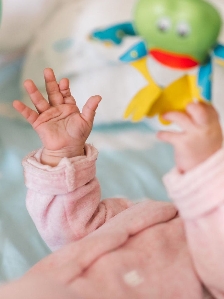 Ein Baby liegt auf dem Rücken unter einem Spielbogen und spielt.