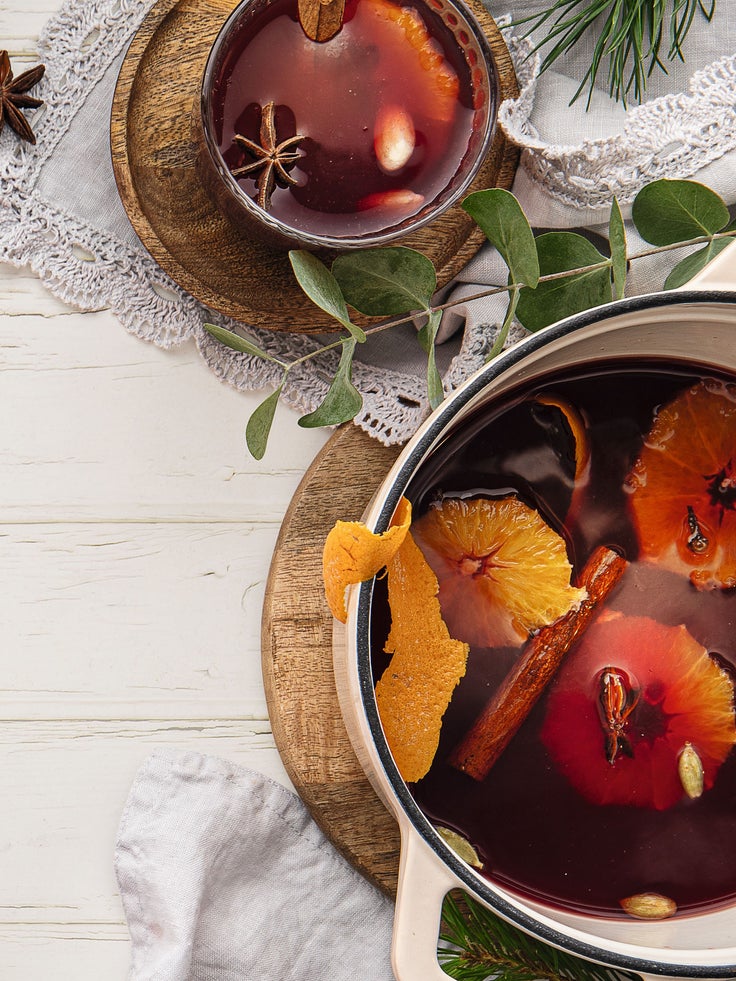 Abgebildet sind ein Topf und eine Tasse gefüllt mit Glögg und Orangenscheiben und Zimtstange