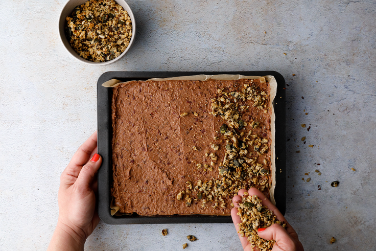 Teig für Protein Bohnenbrownies wird in einer Backform glatt gestrichen und mit Granola bestreut.