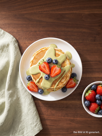 Protein Pancakes mit cremigem Topping, Erdbeeren und Blaubeeren auf einem Teller angerichtet.