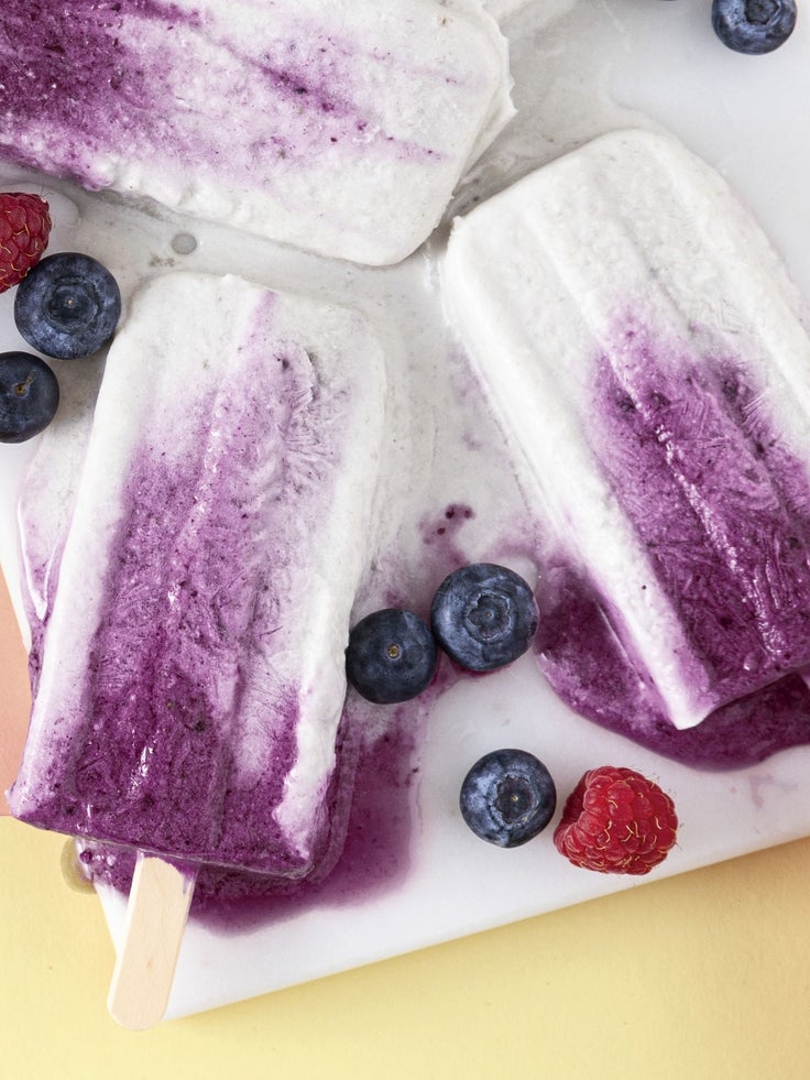 Lila-weiße Beeren-Eis am Stiel auf einem Teller, dekoriert mit Himbeeren und Blaubeeren.