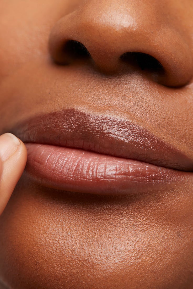 Nahaufnahme einer Person, die mit der Fingerspitze ihre glänzend gepflegten Lippen berührt und so die Wirkung eines Treat & Tint Lippenpflegeprodukts zeigt.
