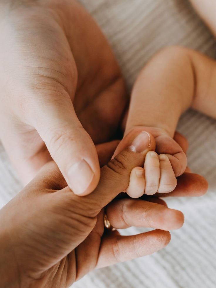 Ein Ausschnitt mit einem Arm eines Babys, die Hand wird von 2 erwachsenen Händen gehalten