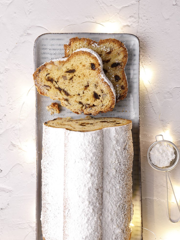 Abgebildet ist ein schmaler Teller mit einem klassischen Stollen bestäubt mit Puderzucker
