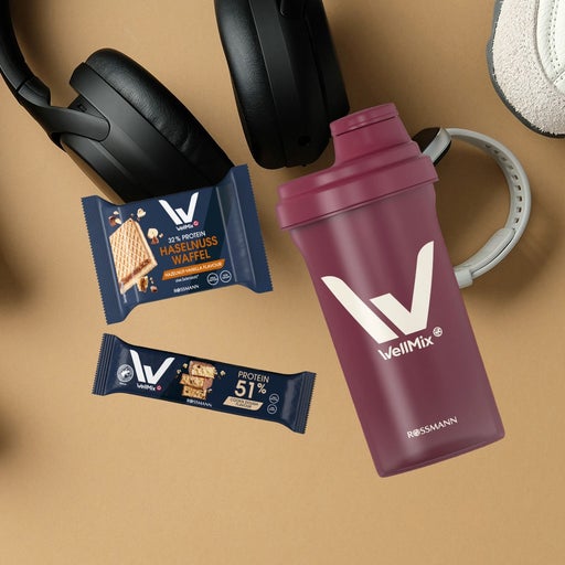 WellMix Shaker, Proteinriegel und Haselnusswaffel zwischen Hanteln, Kopfhörern und Sneakers für Sport und Fitness