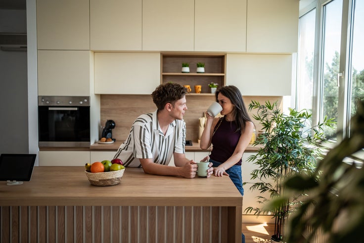 Mann und Frau unterhalten sich entspannt an einer Küchentheke bei einer Tasse Kaffee in einem hell eingerichteten Zuhause.