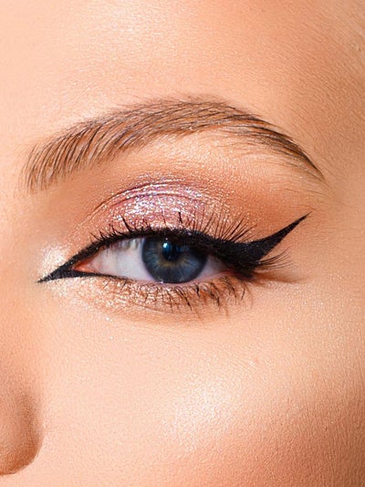Eyeliner ziehen: Nahaufnahme eines Auges mit schwarzem Cat-Eye-Lidstrich, schimmerndem rosé-goldenem Glitzerlidschatten und definierter Augenbraue