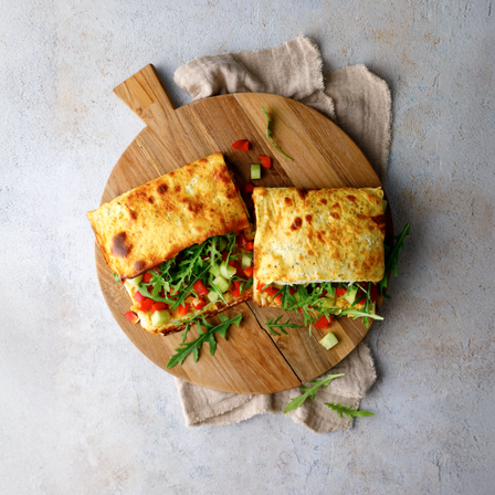 Protein Wraps mit Hummus, Rucola, Gurke und Paprika auf einem runden Holzbrett angerichtet.