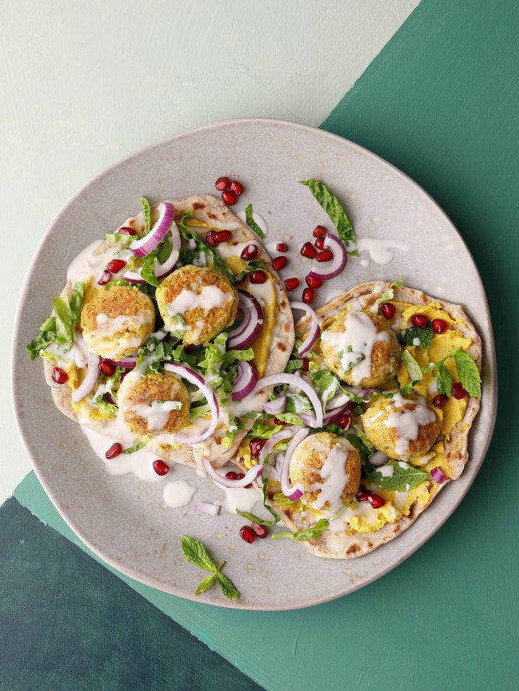 Ein hellgrauer Teller mit Falafel, Salat und Sesamsauce, garniert mit Granatapfelkernen