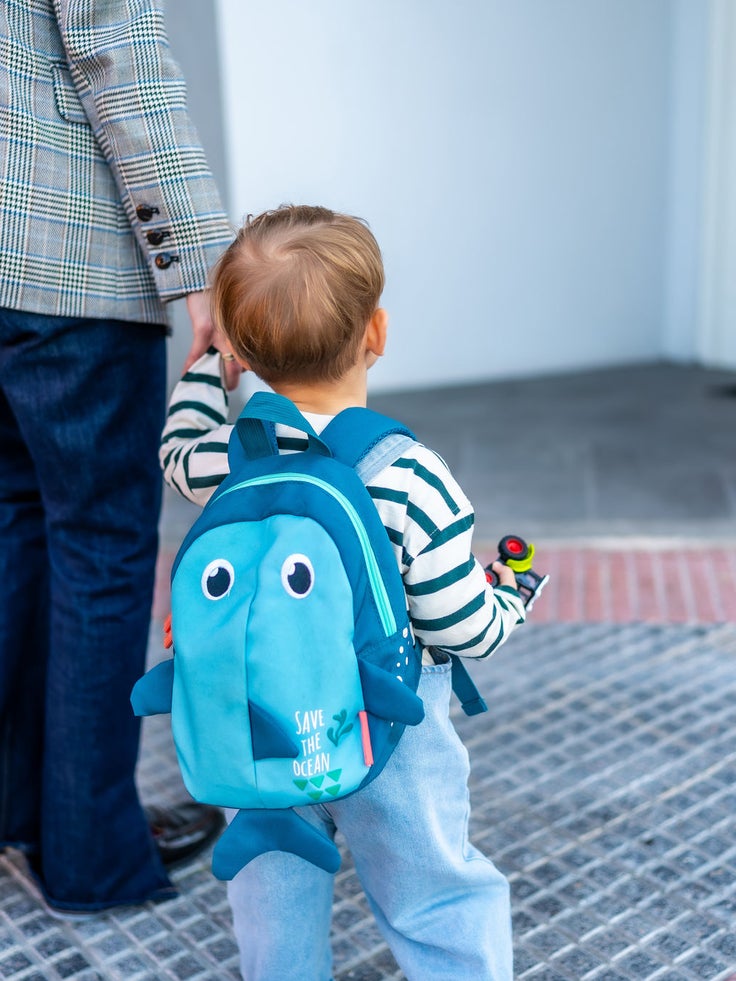 Kleinkind mit blauem Rucksack geht an der Hand einer erwachsenen Person zu einem Hauseingang