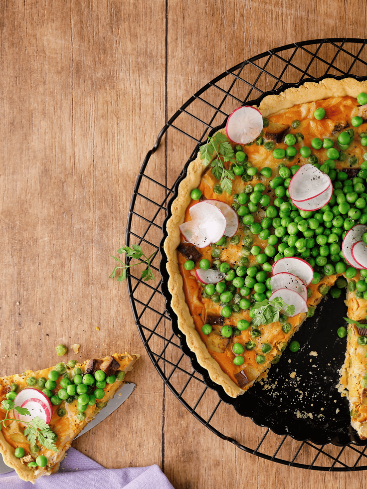 Bildausschnitt ein Kuchengitters, auf dem eine Erbsenquiche liegt, ein Stück ist herausgeschnitten und liegt daneben