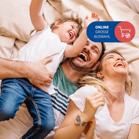 Eine Familie liegt lachend auf einem Bett.