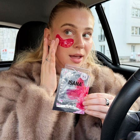 Eine Frau sitzt im Auto und wendet eine Augenmaske an.