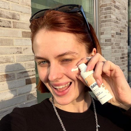 Eine Frau lächelt und hält ein Beispielprodukt von ISANA in der Hand.