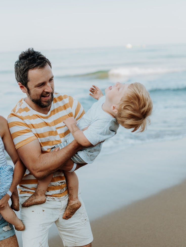 A family with two toddler children walking on beach on summer holiday at sunset.
