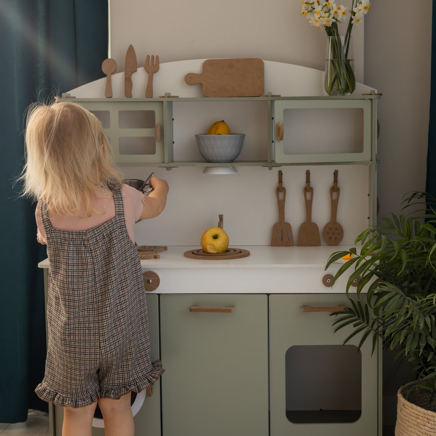 Kleinkind spielt an einer Kinderküche mit Holzspielzeug und Obst in einem hellen Wohnraum