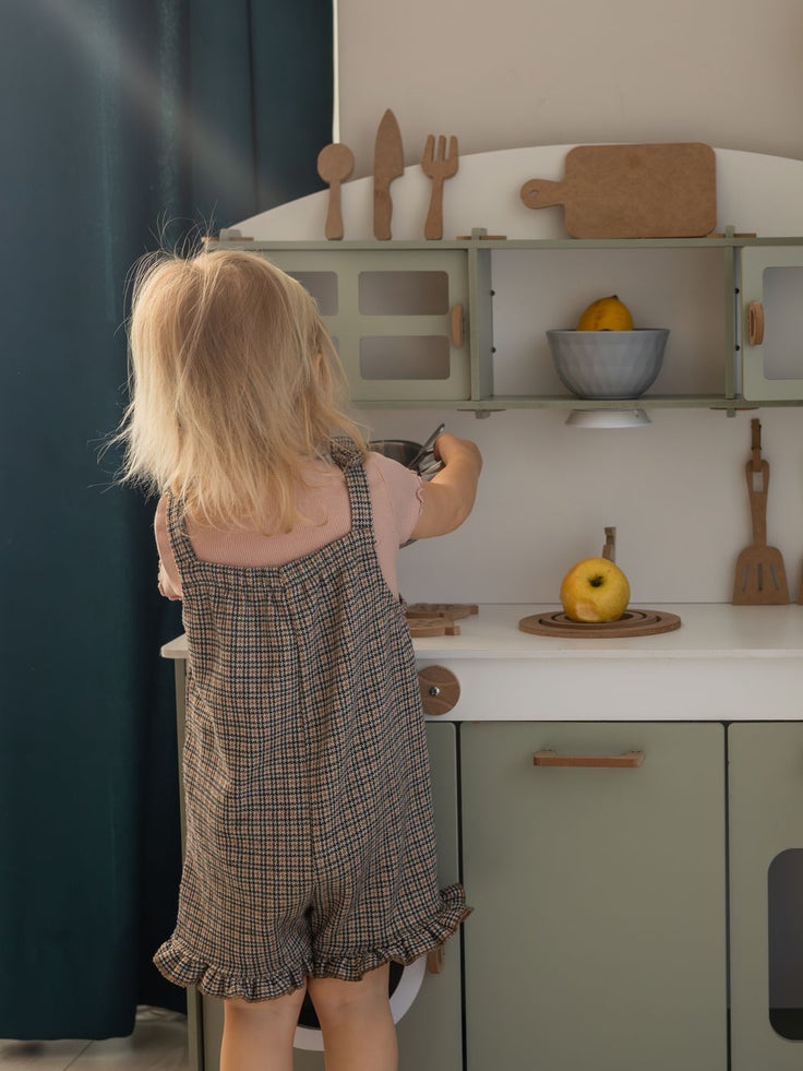 Kleinkind spielt an einer Kinderküche mit Holzspielzeug und Obst in einem hellen Wohnraum