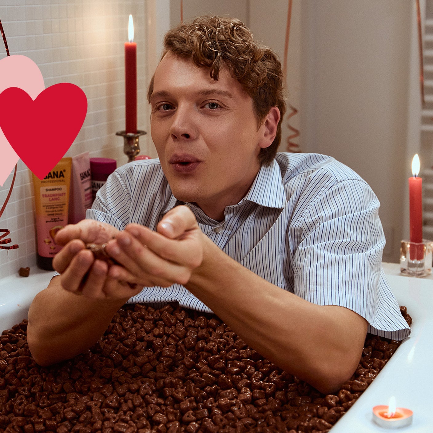 Ein Mann hockt vor einer Badewanne, befüllt mit vielen Schokoladenherzen.