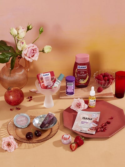 Auswahl an ISANA und Alterra Pflegeprodukten mit Granatapfel, Beeren und Rosen dekoriert