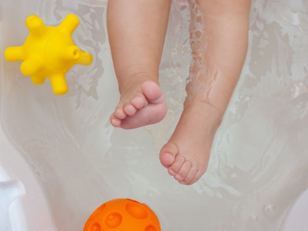 Kleine Babyfüße in einer Badewanne mit Spielzeug in der Wanne.