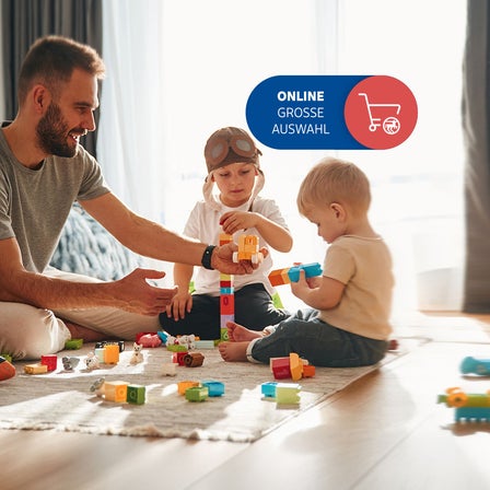 Ein Vater spielt mit zwei Kindern auf dem Boden.