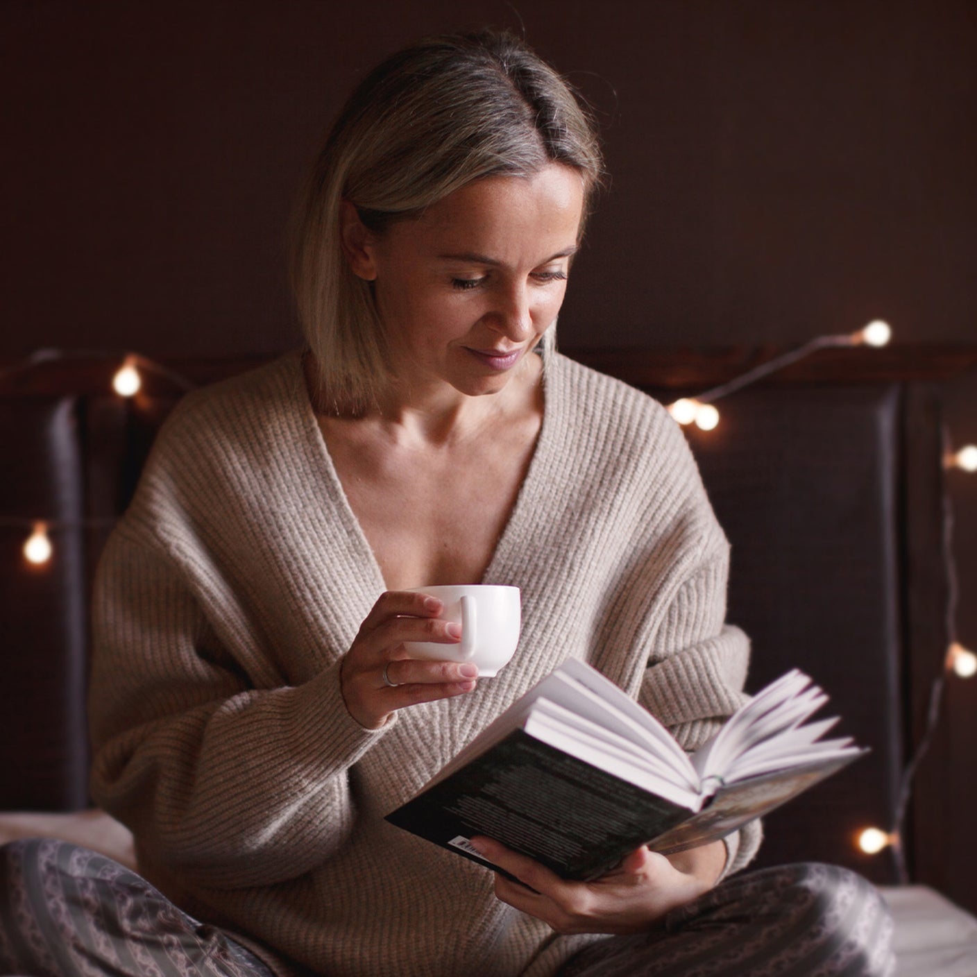 Eine Frau sitzt auf dem Bett und liest ein Buch bei schöner Beleuchtung