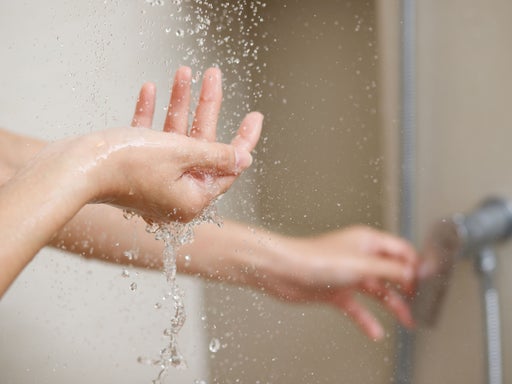  Eine Frau steht unter der Dusche und stellt an der Armatur die Temperatur ein. Währenddessen kontrolliert sie die Temperatur mit ihrer Hand.