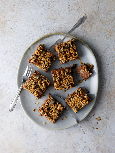 Protein Bohnenbrownies in Quadraten mit knusprigem Granola-Topping auf einem Teller auf grauem Hintergrund angerichtet.