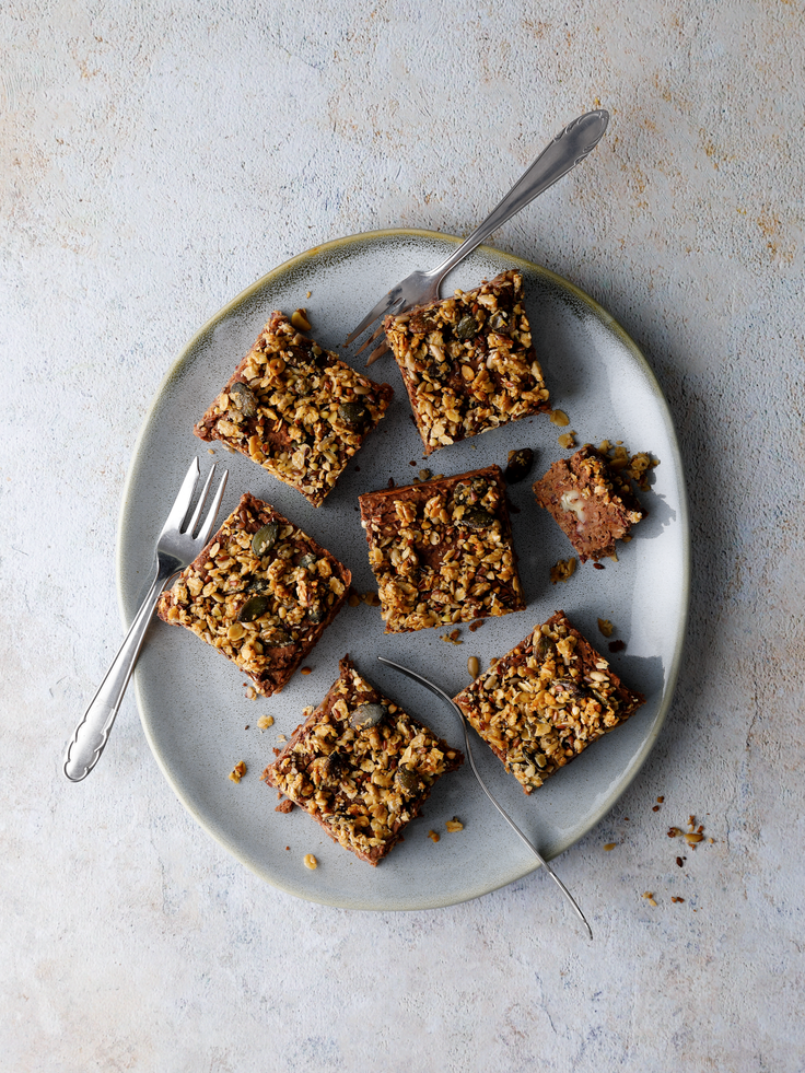 Protein Bohnenbrownies in Quadraten mit knusprigem Granola-Topping auf einem Teller auf grauem Hintergrund angerichtet.