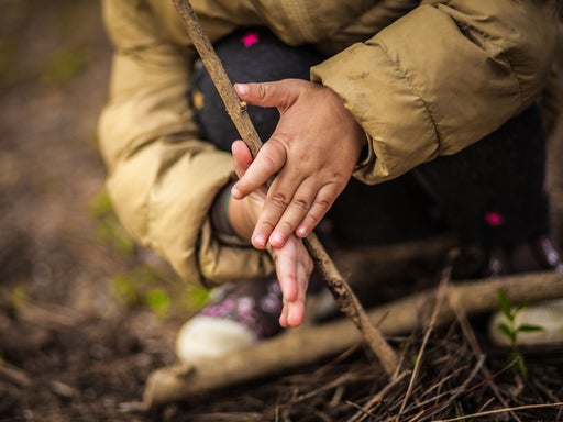 Kleine Kinderhände in beigefarbener Winterjacke greifen neugierig nach einem rauen Naturseil bei einer Sinneserfahrung im Freien