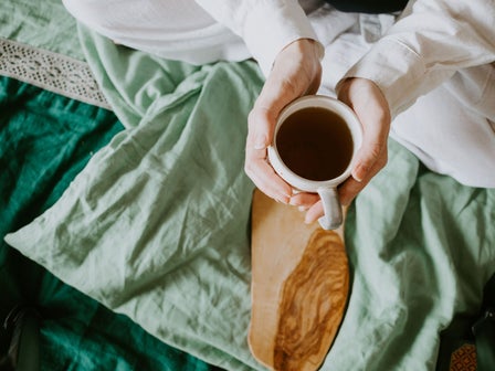 Person hält eine Tasse Tee im Bett und schafft einen ruhigen Moment im Familienalltag