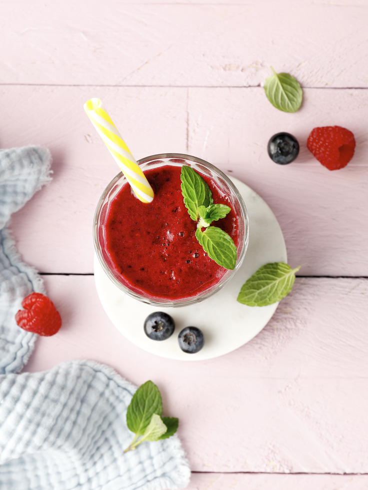 Roter Beeren-Smoothie mit Himbeeren, Heidelbeeren und Minze im Glas auf rosa Holzuntergrund