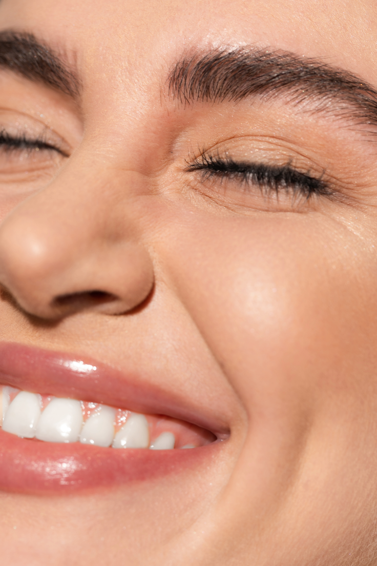 Nahaufnahme eines lächelnden Gesichts mit natürlichem Make-up, definierten Brauen, getuschten Wimpern und glänzenden Lippen für einen frischen Morgen-Glow.