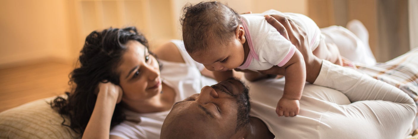 Eltern liegen mit ihrem Baby auf dem Bett und genießen einen ruhigen Familienmoment zu Hause
