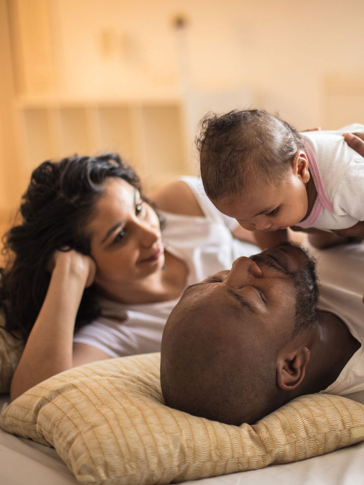 Eltern liegen mit ihrem Baby auf dem Bett und genießen einen ruhigen Familienmoment zu Hause