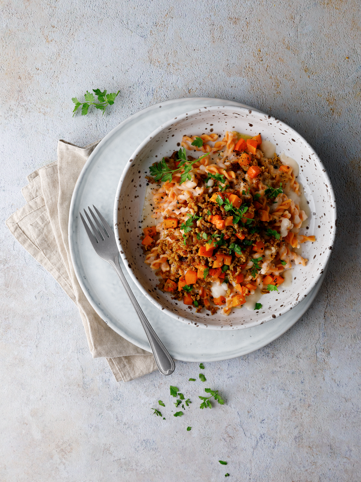 Protein Linsen-Spirelli mit Bohnensauce, Gemüsewürfeln und Kräutern in einer Schale auf hellem Teller angerichtet.